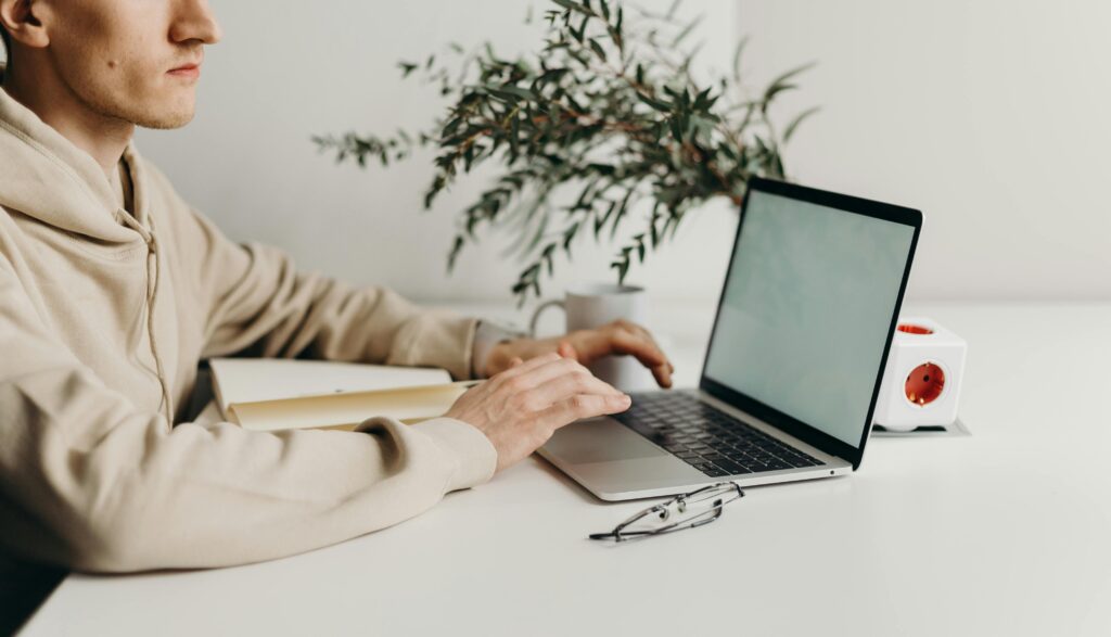 Person sitting at a desk using a laptop with a notebook beside them, representing a small business owner working on local SEO strategies.